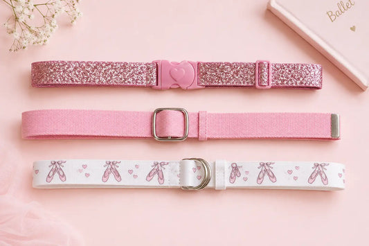Three girls belts including pink sparkle, solid pink canvas and ballet shoes design laid flat on a pastel background